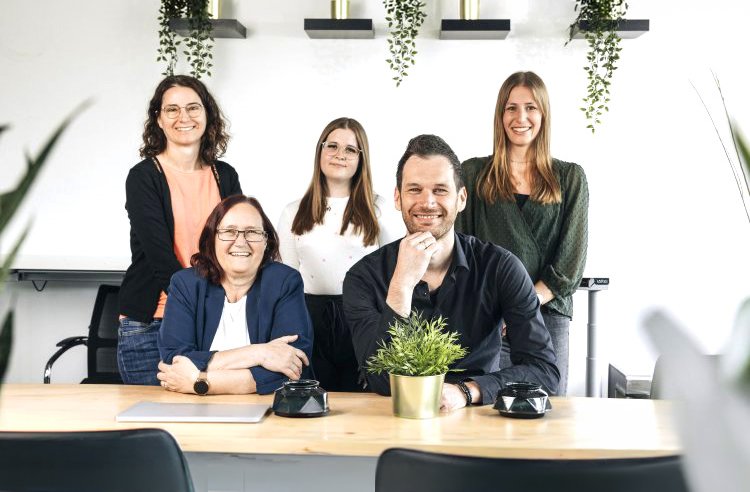Team - Alle Mitarbeiter hinter einem Schreibtisch, Blick in die Kamera